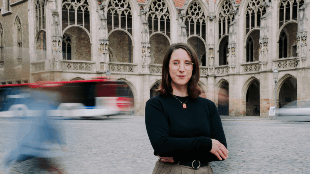 Swantje Schendel steht auf dem Altstadtmarkt in Braunschweig und schaut dich entschlossen an. Im Hintergrund das alte Rathaus, ein Bus fährt und Passanten gehen vorbei.